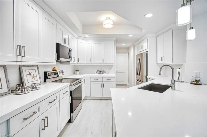 Kitchen with stainless steel appliances, light stone countertops, hanging light fixtures, a tray ceiling, and white cabinets