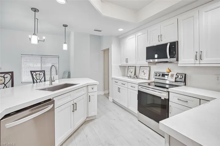 Kitchen featuring appliances with stainless steel finishes, white cabinetry, decorative light fixtures, recessed lighting, and light wood-style flooring