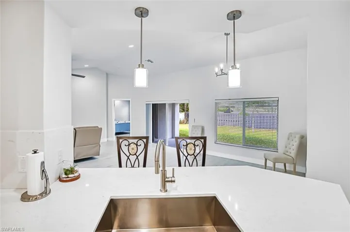 Kitchen featuring light stone counters, decorative light fixtures, wood finished floors, open floor plan, and vaulted ceiling