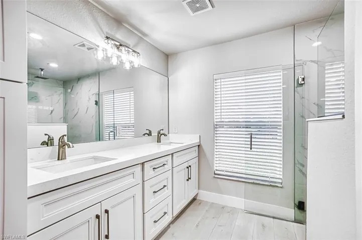 Full bath with a marble finish shower, double vanity, and light wood-style floors