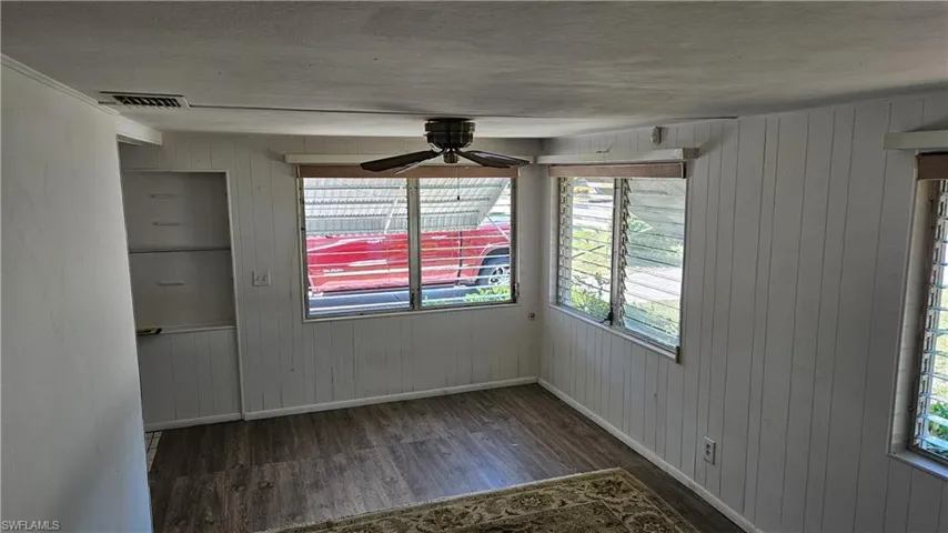 Empty room with wood finished floors, baseboards, a ceiling fan, and wood walls