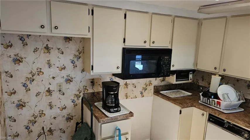 Kitchen with black microwave, white dishwasher, dark countertops, cream cabinetry, and tasteful backsplash