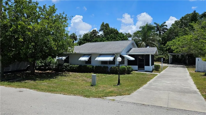 Ranch-style home with a front yard, concrete driveway, a shingled roof, and a carport