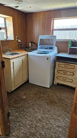 Washroom with washer / dryer, wood walls, dark carpet, and a sink
