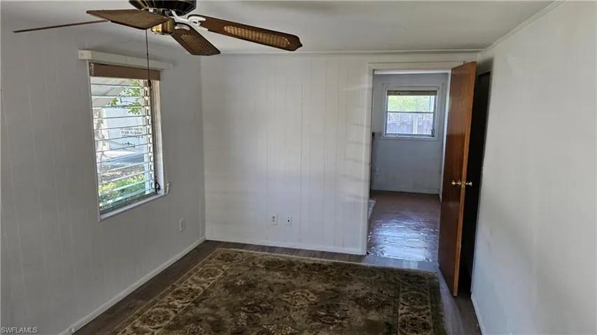 Unfurnished room with wood finished floors, a ceiling fan, baseboards, and wood walls