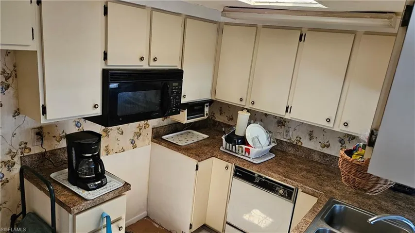 Kitchen featuring black microwave, white dishwasher, decorative backsplash, and cream cabinets