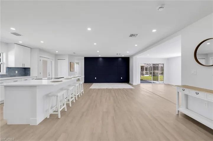 Kitchen with light wood-style flooring, visible vents, white cabinets, a large island, and tasteful backsplash