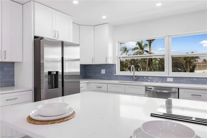 Kitchen with stainless steel appliances, a sink, white cabinetry, light countertops, and decorative backsplash