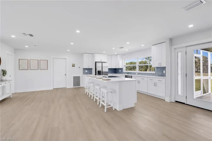 Kitchen with a breakfast bar, visible vents, light wood-style floors, stainless steel refrigerator with ice dispenser, and tasteful backsplash