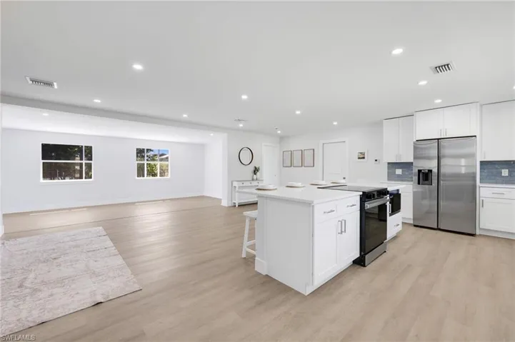 Kitchen with electric range, visible vents, open floor plan, stainless steel refrigerator with ice dispenser, and decorative backsplash