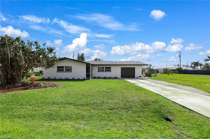Ranch-style home with driveway, an attached garage, a front lawn, and stucco siding