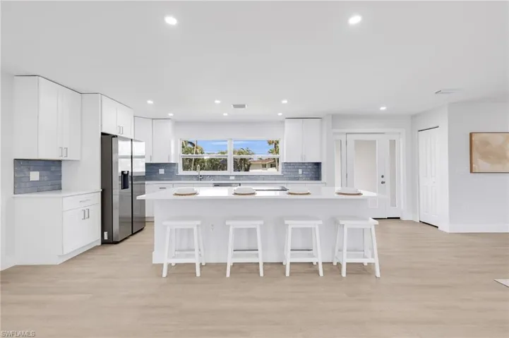 Kitchen featuring a breakfast bar, light countertops, stainless steel refrigerator with ice dispenser, and white cabinetry