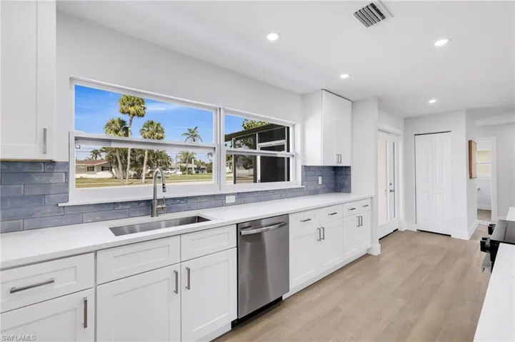 Kitchen featuring visible vents, white cabinets, stainless steel dishwasher, light wood-style floors, and a sink
