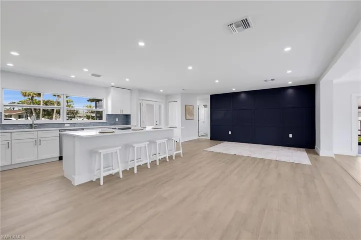 Kitchen with visible vents, light wood-style flooring, decorative backsplash, white cabinets, and an island with sink