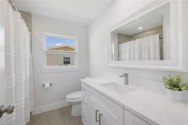 Full bathroom with curtained shower, toilet, wood finished floors, vanity, and baseboards