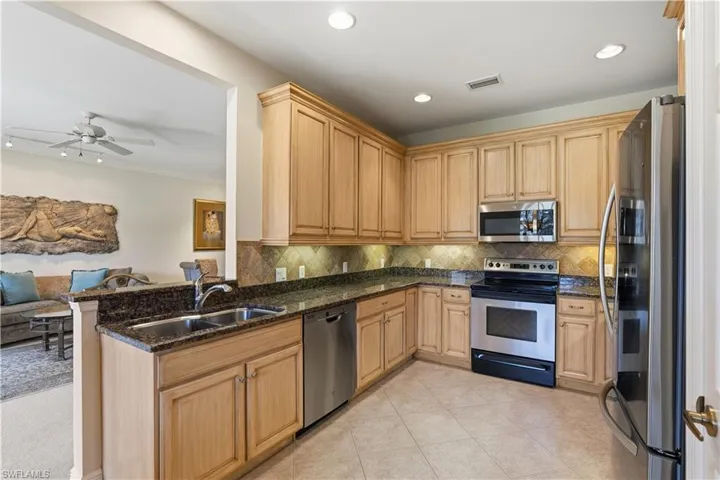 Kitchen featuring wood cabinetry, stainless steel appliances, dark stone countertops, tile backsplash, and recessed lighting