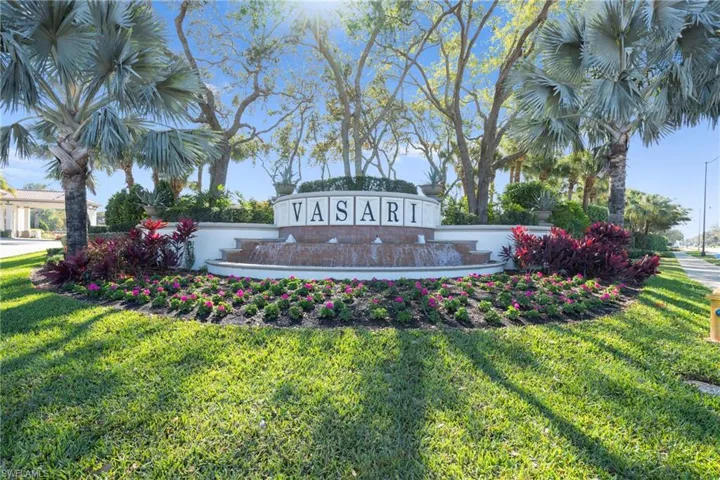 Community entrance featuring a tiered fountain, lush landscaping, and mature palm trees