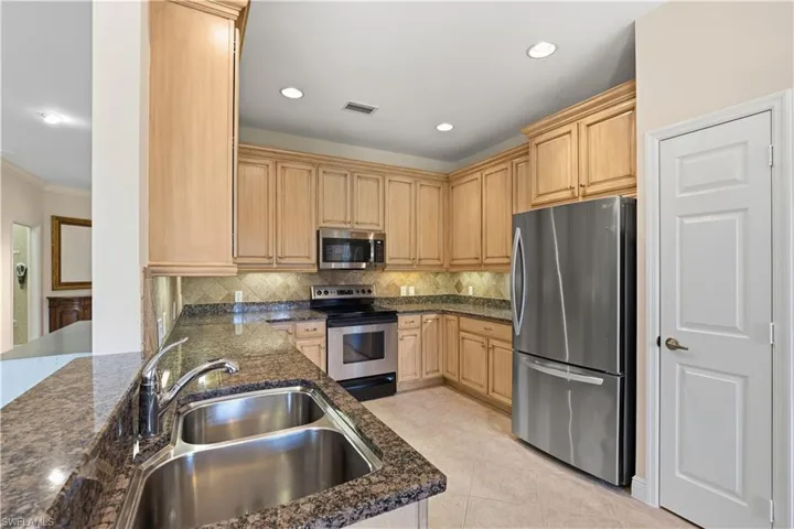 Kitchen featuring wood cabinetry, stainless steel appliances, a dual-basin sink, granite countertops, and recessed lighting