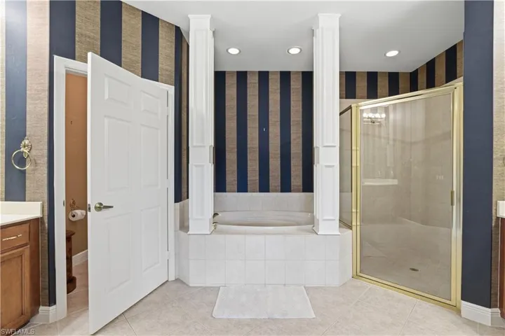 Soaking tub with tile surround, separate shower with framed glass enclosure, dual vanities with wood cabinetry, and recessed lighting