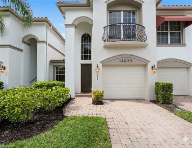 Stucco exterior with arched entryways, decorative iron balcony, paved driveway, and multiple garage doors