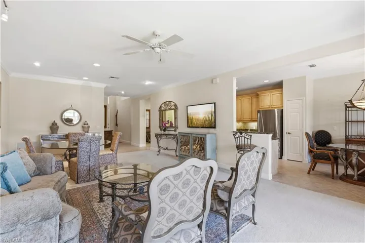Recessed lighting and a ceiling fan illuminate a spacious living area with neutral-toned walls