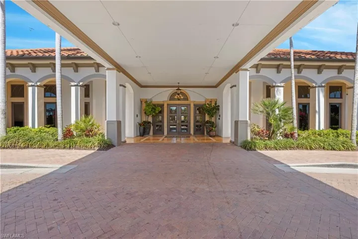 Covered portico entrance with a paver driveway, decorative arched windows, and lush landscaping