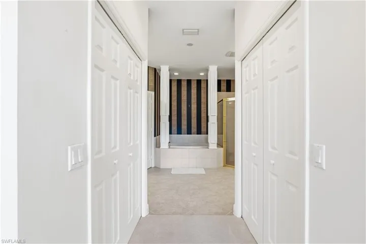 Spacious hallway with dual white six-panel closet doors, neutral tile flooring, and recessed ceiling lighting
