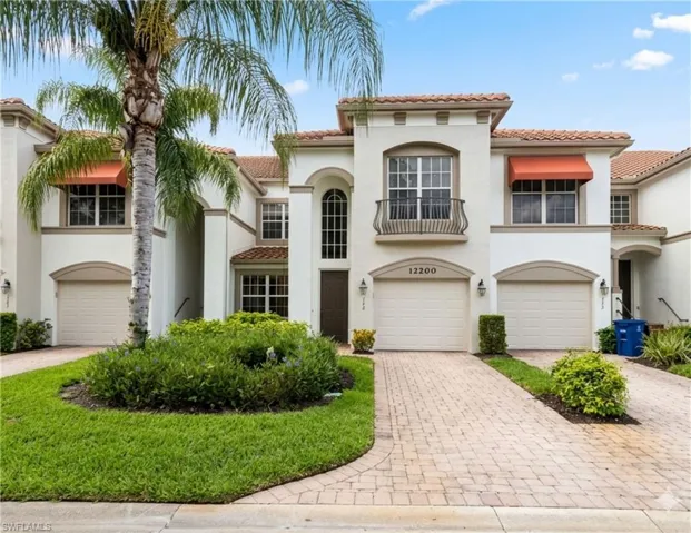 Stucco exterior featuring multiple orange awnings, two garage doors, an arched entry, and a prominent palm tree
