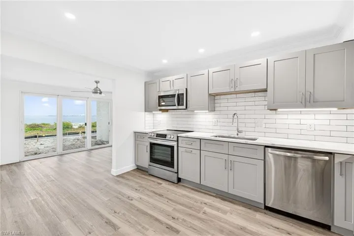 Kitchen featuring gray cabinets, appliances with stainless steel finishes, crown molding, tasteful backsplash, and light wood-style flooring