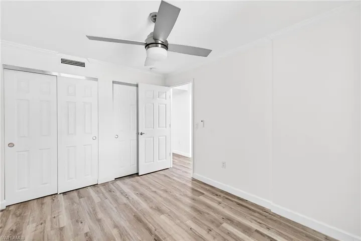 Unfurnished bedroom featuring ornamental molding, light wood-type flooring, two closets, and a ceiling fan