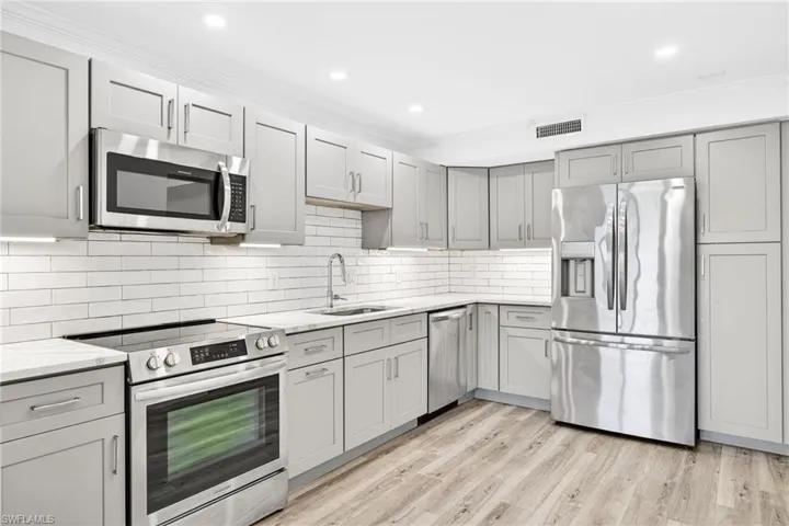 Kitchen with appliances with stainless steel finishes, gray cabinetry, ornamental molding, light wood finished floors, and backsplash