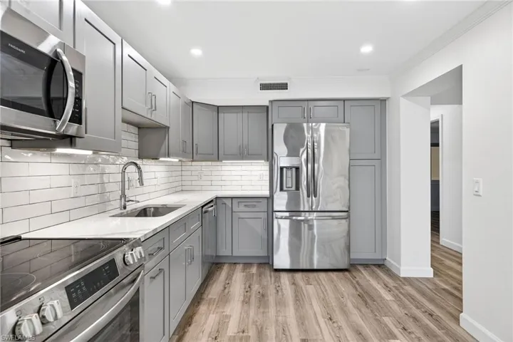 Kitchen with gray cabinets, stainless steel appliances, crown molding, light stone countertops, and decorative backsplash