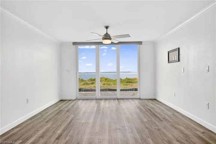Living room with expansive windows, a water view, light wood-style floors, a ceiling fan, and ornamental molding
