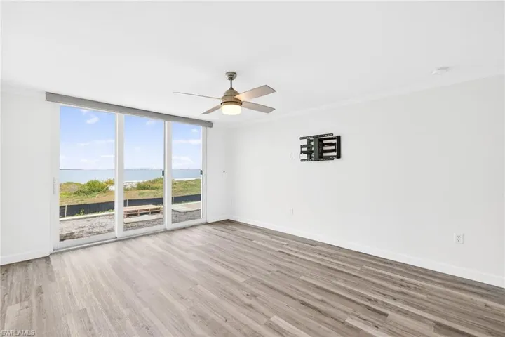 Primary bedroom with a water view, a wall of windows, ornamental molding, light wood-type flooring, and ceiling fan