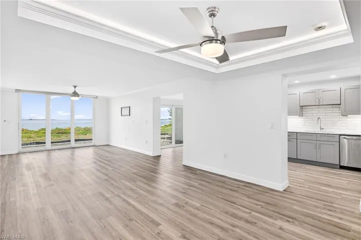 Unfurnished living room with ceiling fan, ornamental molding, light wood-type flooring, a water view, and a raised ceiling