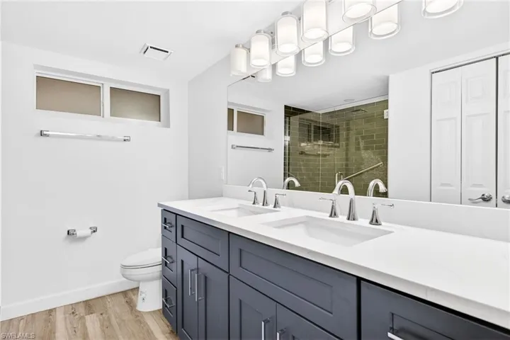 Primary bathroom with double vanity, a stall shower, light wood finished floors, and a closet