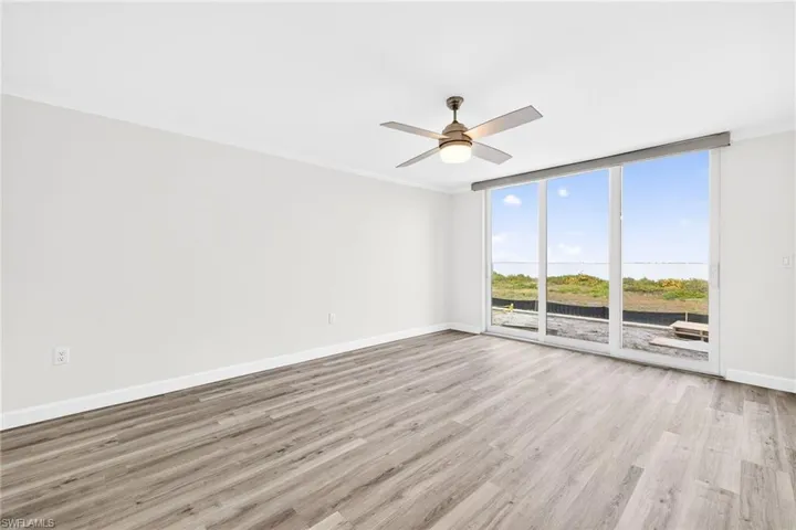 Living room with light wood-type flooring, ornamental molding, a wall of windows, and a ceiling fan