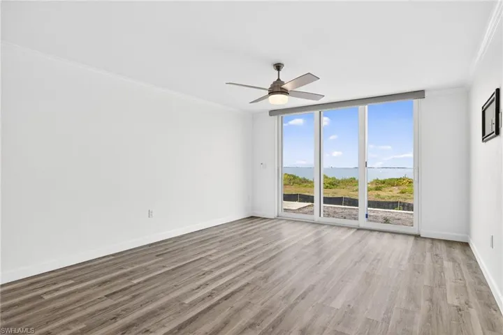Living room with a water view, expansive windows, crown molding, light wood-type flooring, and a ceiling fan