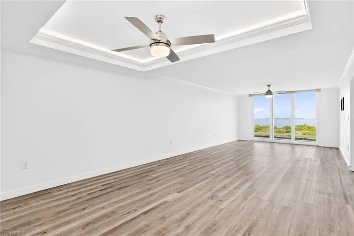 Dining/Living combo featuring expansive windows, light wood-style floors, a tray ceiling, ceiling fan, and ornamental molding