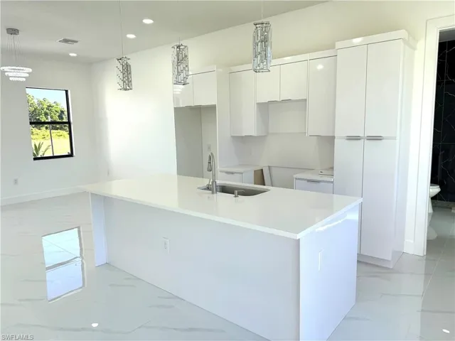 Kitchen featuring light marble finish flooring, white cabinetry, modern cabinets, a center island with sink, and recessed lighting