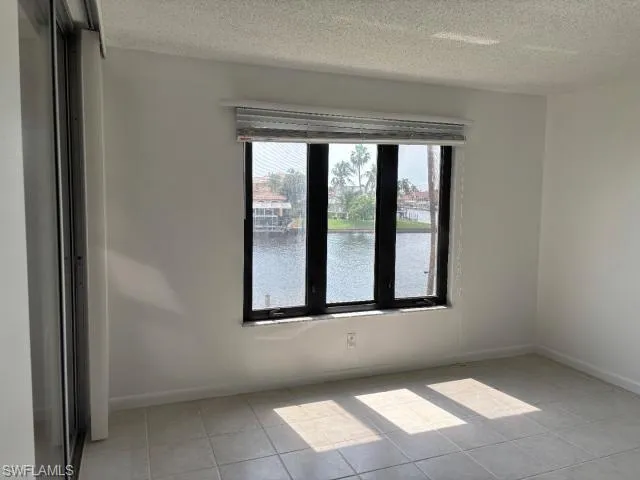 Unfurnished room featuring a water view, a textured ceiling, and light tile patterned floors