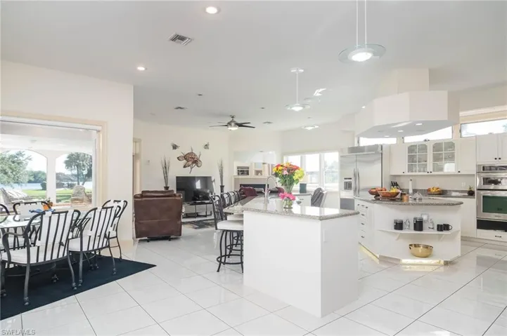 Big open kitchen with white wood cabinetry, large island with glass block accent lighting, long breakfast bar, lots of recessed lighting, Kitchenaid Stainless Appliances and lots of natural light.
