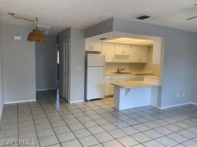 Kitchen with a breakfast bar area, white refrigerator, sink, kitchen peninsula, and light tile patterned flooring