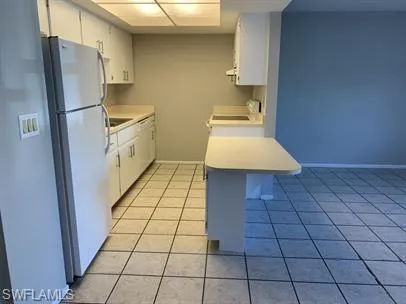 Kitchen with kitchen peninsula, white cabinetry, white refrigerator, and light tile patterned floors