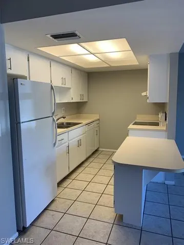 Kitchen with sink, white cabinetry, light tile patterned floors, and white appliances