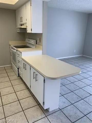 Kitchen with a textured ceiling, range with electric stovetop, white cabinetry, and light tile patterned flooring