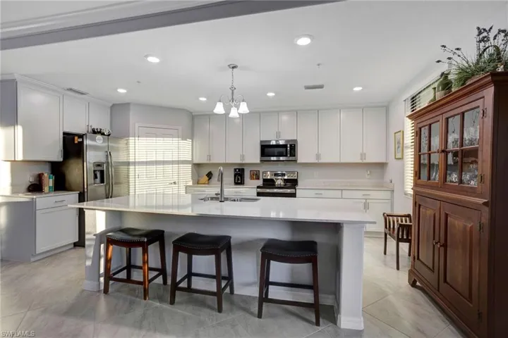 Kitchen with stainless steel appliances, a breakfast bar, white cabinetry, hanging lights, and an island with sink