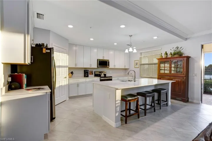 Kitchen with a breakfast bar area, stainless steel appliances, an island with sink, white cabinets, and crown molding
