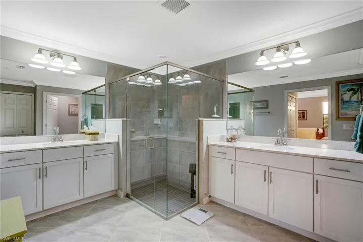Ensuite bathroom with crown molding, two vanities, a shower stall, and light tile patterned flooring
