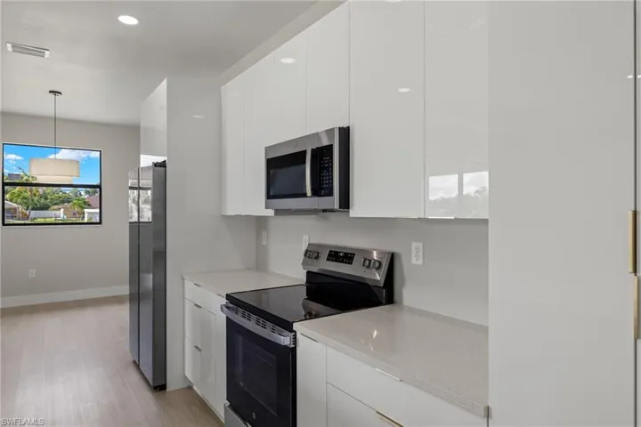 Kitchen with light stone counters, appliances with stainless steel finishes, white cabinets, and light hardwood / wood-style floors